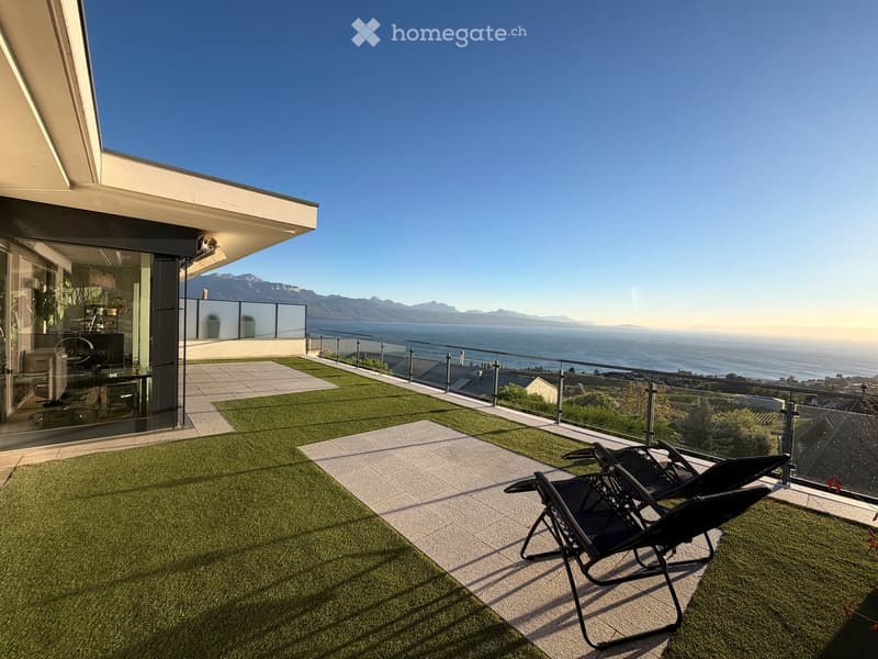 Modern rooftop terrace with artificial grass, sun loungers, and a panoramic view of the sea and mountains.