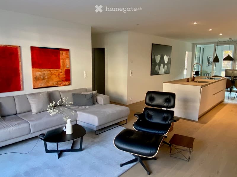 white walls, wooden floor, grey couch, coffee table, black chair, sink, countertop, kitchen