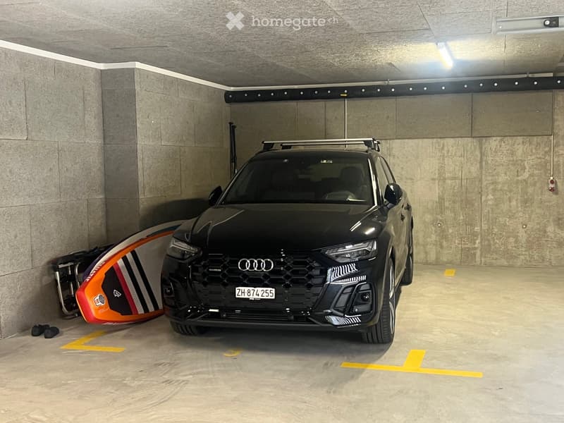 Black Audi SUV parked in a parking garage with a surfboard and shoes nearby