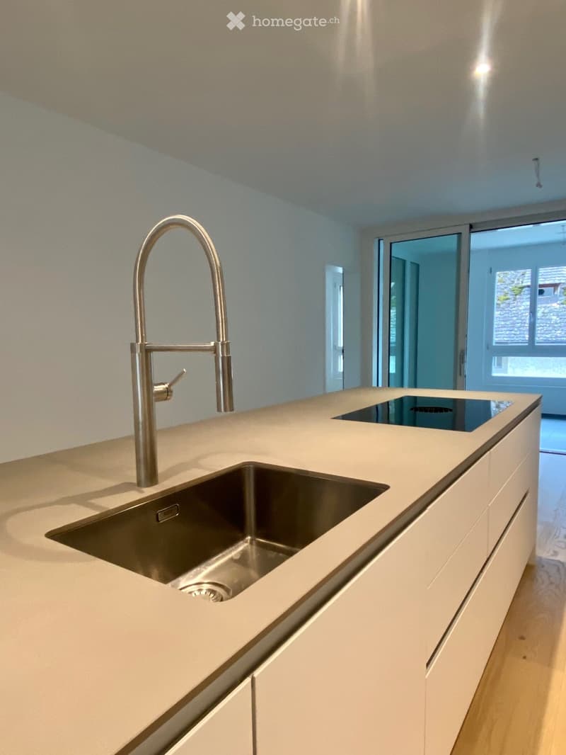 Modern kitchen with white cabinetry, silver kitchen island, stainless steel faucet, induction cooktop, and glass slider doors to a balcony.