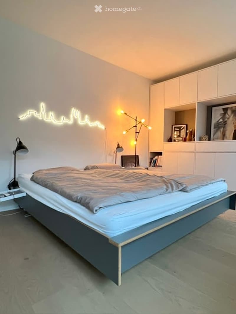 Modern bedroom with a large bed, nightstand, floor lamp, bookshelf, and decorative picture frame on the wall.