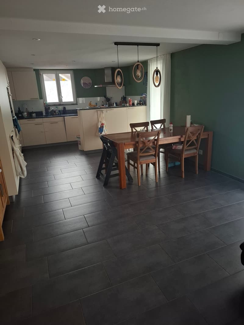 Modern kitchen with dark tiled flooring, light-colored cabinets, and a central dining table with chairs. The kitchen features a sink, refrigerator, and various appliances.
