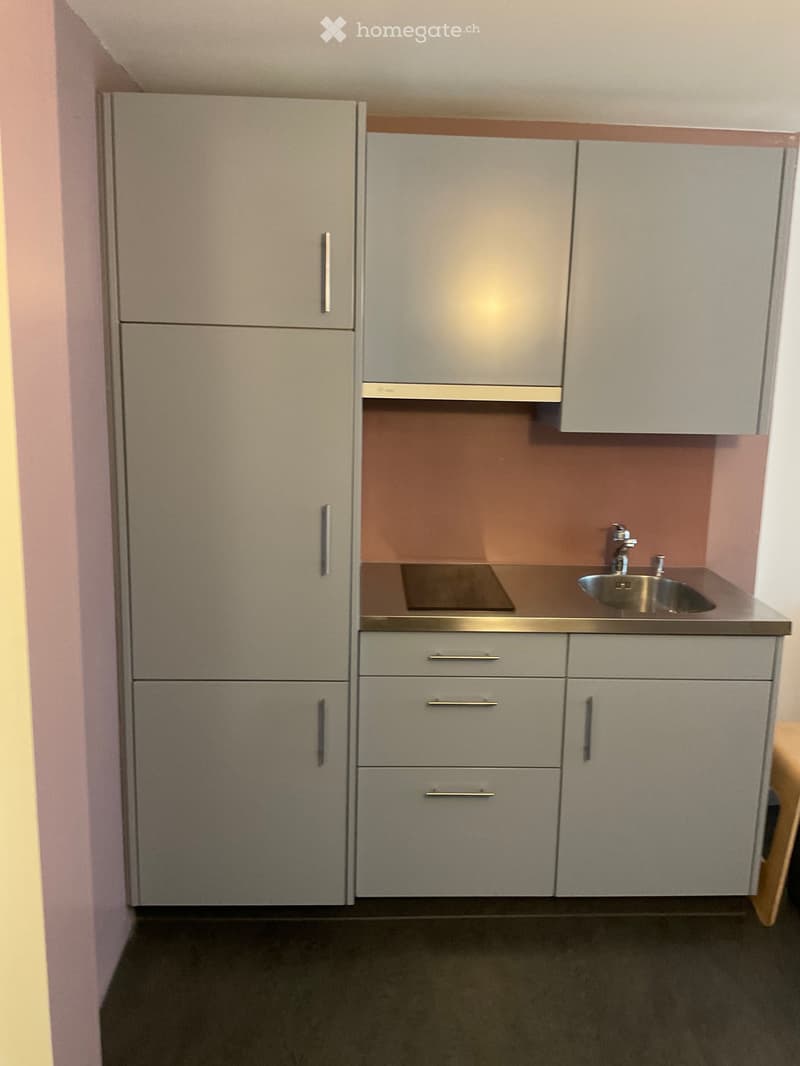 Modern kitchen with grey cabinets, a sink, and a faucet. The backsplash is a warm orange color, and the countertop is sleek and metallic.