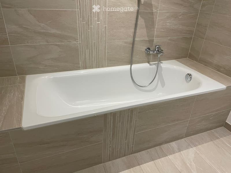 Modern bathroom with a white bathtub, sleek faucet, and grey tiled walls and floor.