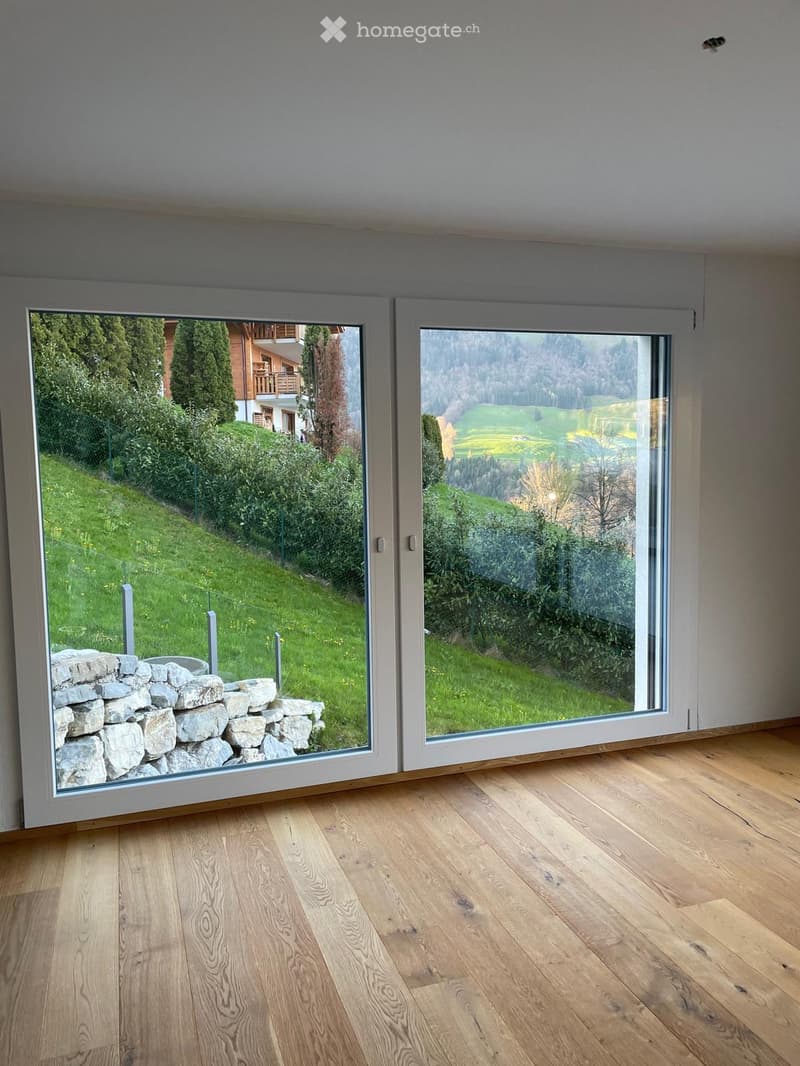 Empty room with wooden flooring and large sliding glass doors opening to a green outdoor area.