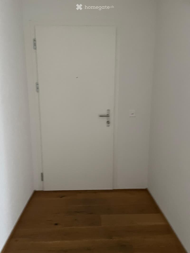 Empty room with wooden floor, white walls, and a closed white door.
