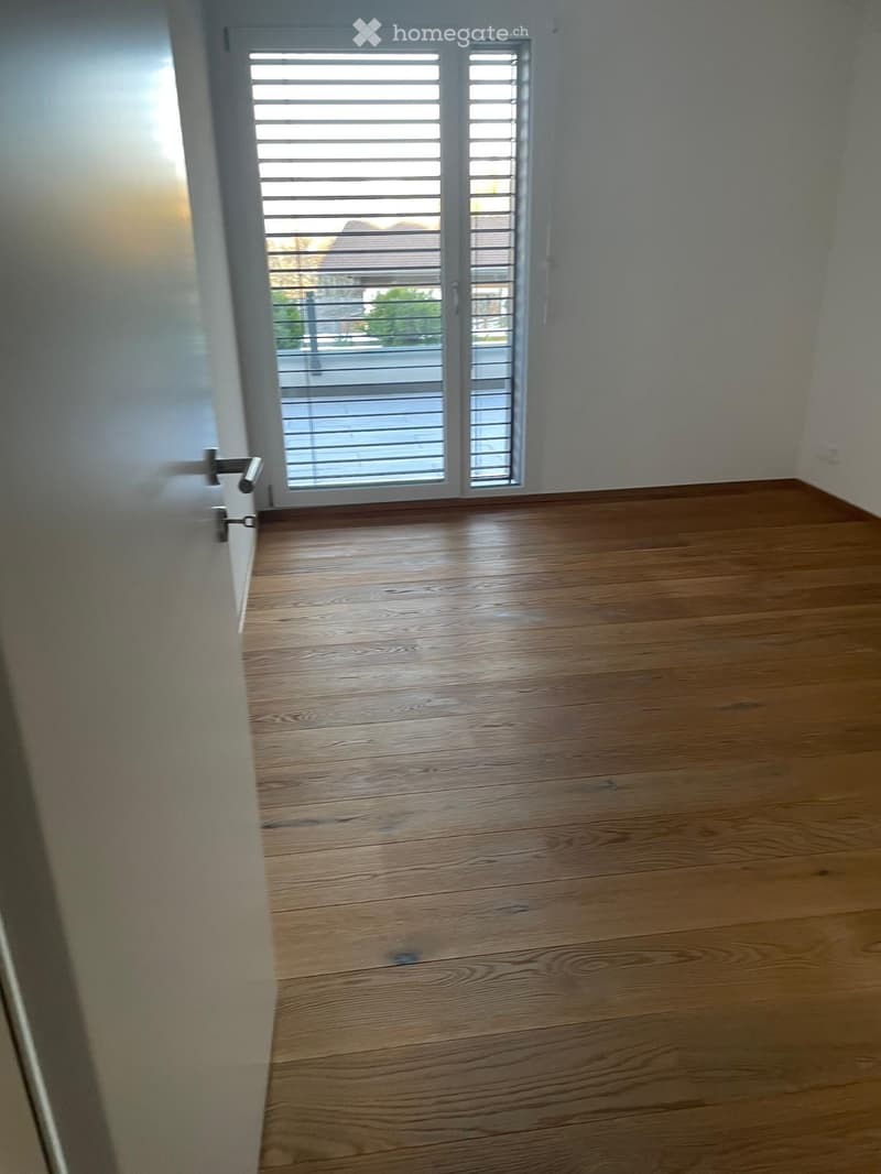 Empty room with wooden flooring and large window with blinds, no furniture or equipment present.