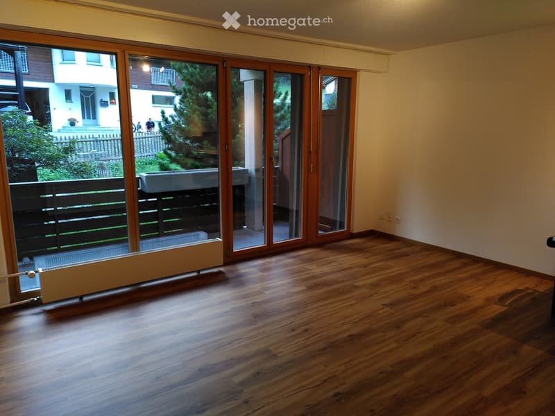 Empty room with wooden flooring, large sliding glass doors leading to a balcony, radiator, and visible outdoor view.