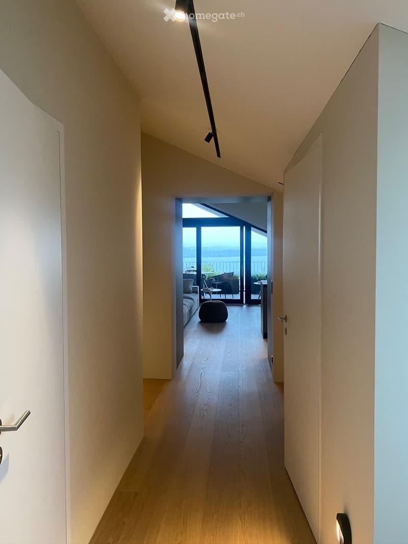 Modern hallway with wooden flooring, recessed lighting, and an open doorway leading to a living area with a view of the water.
