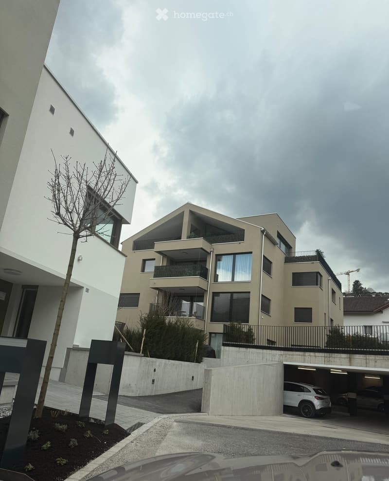 Modern multi-story residential building with balconies, large windows, and a covered parking area.