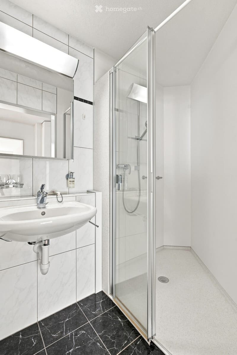 Modern bathroom with a white sink, large mirror, glass-enclosed shower, and marble tiles.