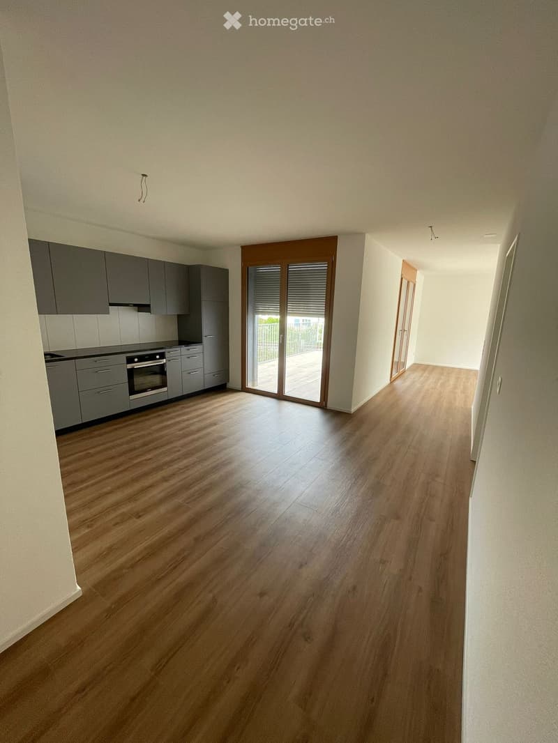Empty room with wooden flooring, grey cabinets, and a sliding glass door leading to a balcony.