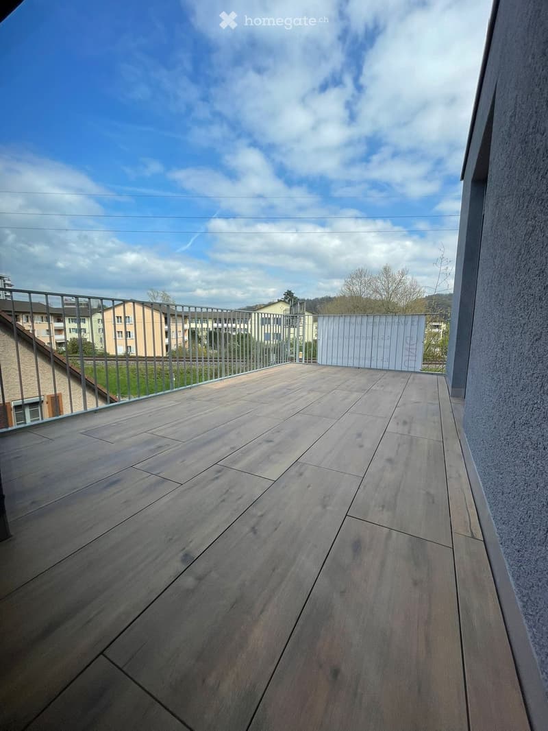 Wooden deck with metal railing, overlooking a residential area with buildings and trees.