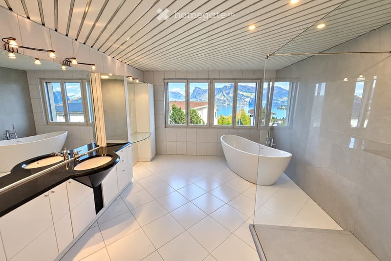Modern bathroom with white tiles, two bathtubs, a double sink, and large windows offering a scenic mountain view.