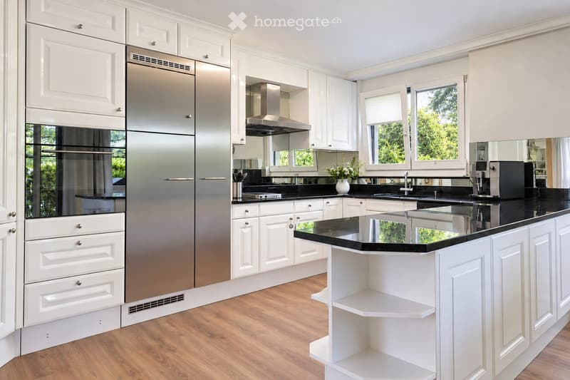 Modern kitchen with white cabinets, stainless steel appliances, black countertops, and a central island.