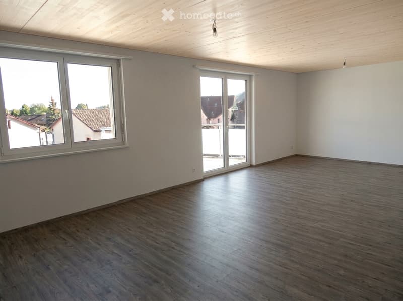 Empty room with wooden flooring, white walls, large windows, and a sliding glass door leading to a balcony.