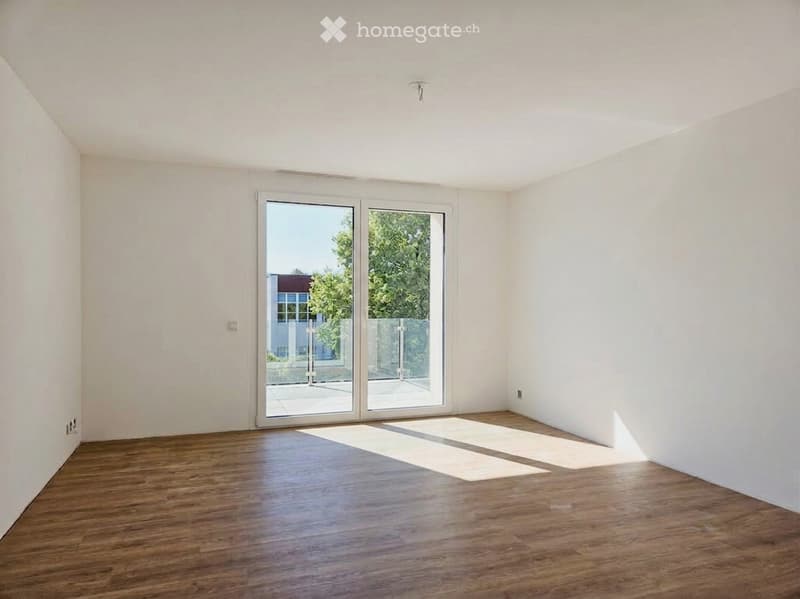Empty room with white walls, wooden flooring, and large sliding glass doors leading to an outdoor area.