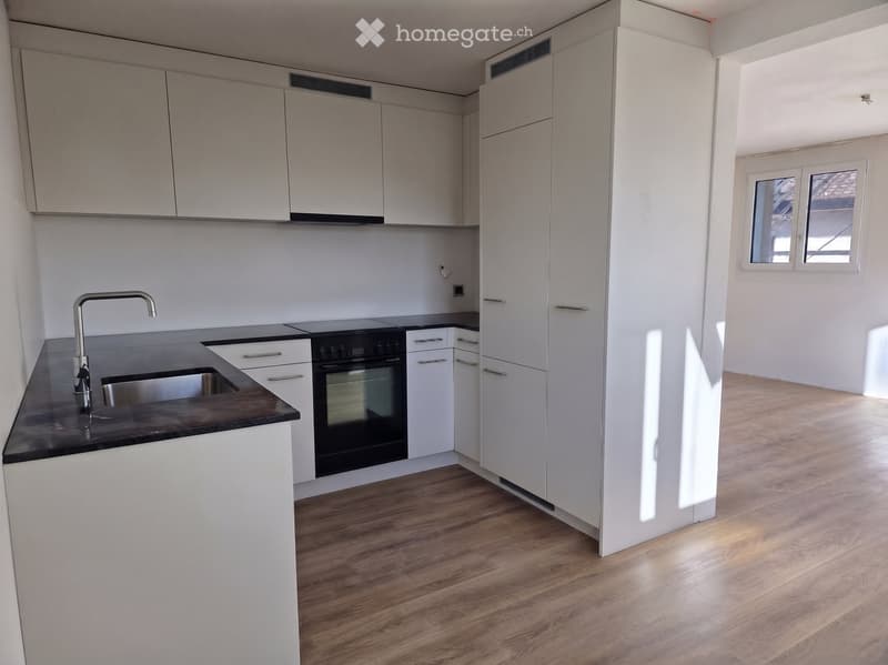 Modern kitchen with white cabinets, dark countertops, and a stainless steel sink and faucet. The floor is wooden, and there is a window on the right side.
