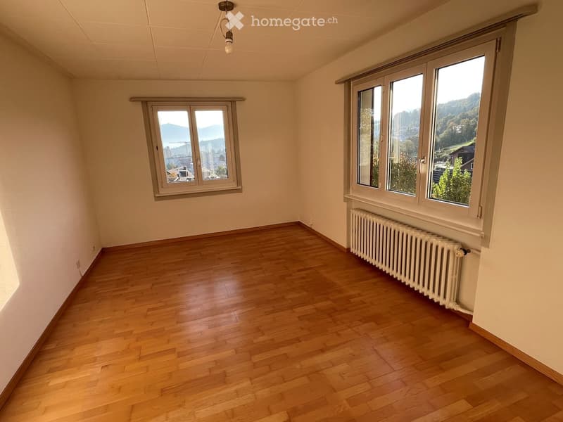 Empty room with wooden flooring, white walls, and large windows offering a scenic view.