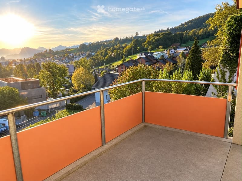 Balcony with orange privacy screens, metal railing, and a scenic view of a town and mountains.