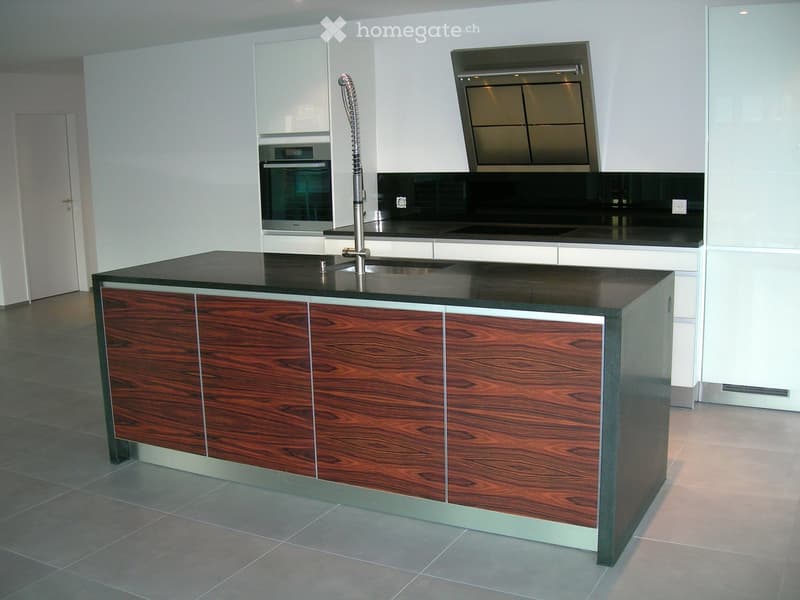 Modern kitchen with a central island, sleek black countertops, and stainless steel appliances including an oven and range hood.