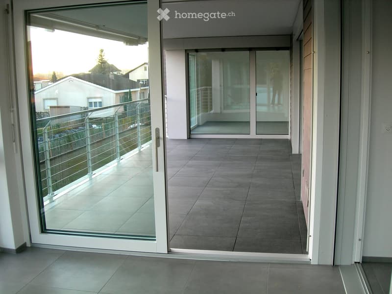 Modern balcony with large glass sliding doors, tiled floor, metal railing, and view of neighboring houses.