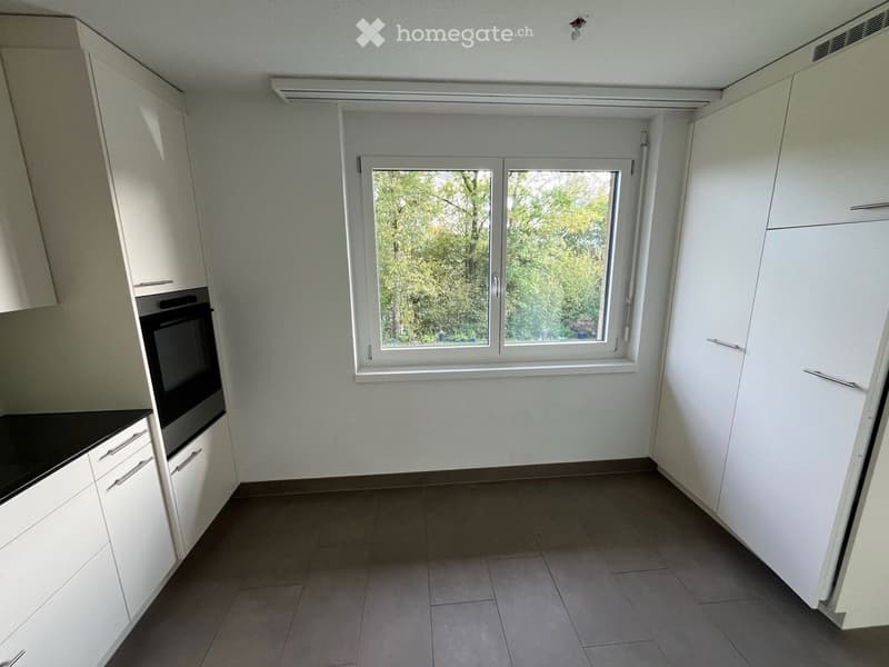 Empty kitchen with white cabinets, black countertop, and a window overlooking greenery.