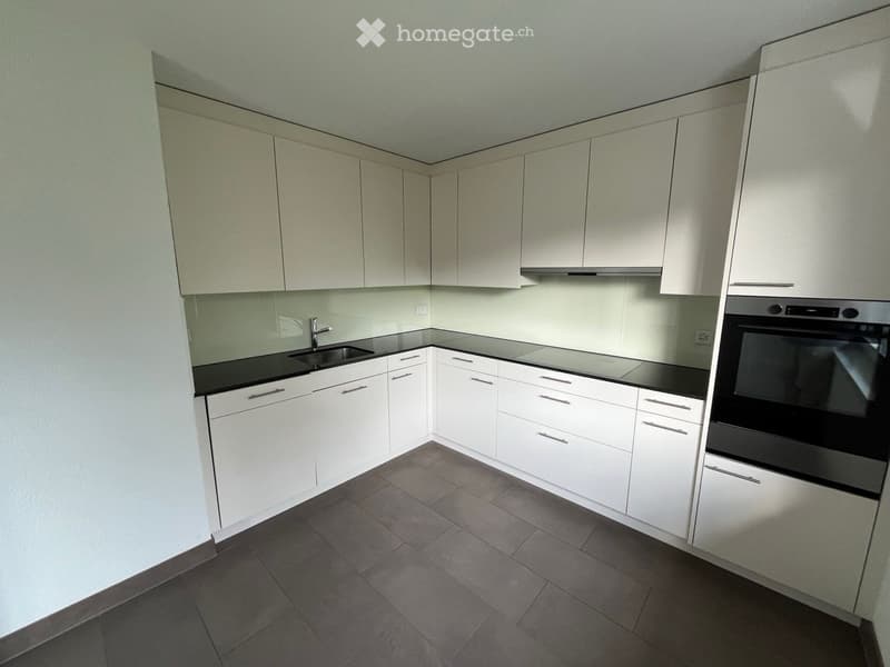 Modern kitchen with white cabinets, black countertops, and stainless steel appliances including a sink and oven.
