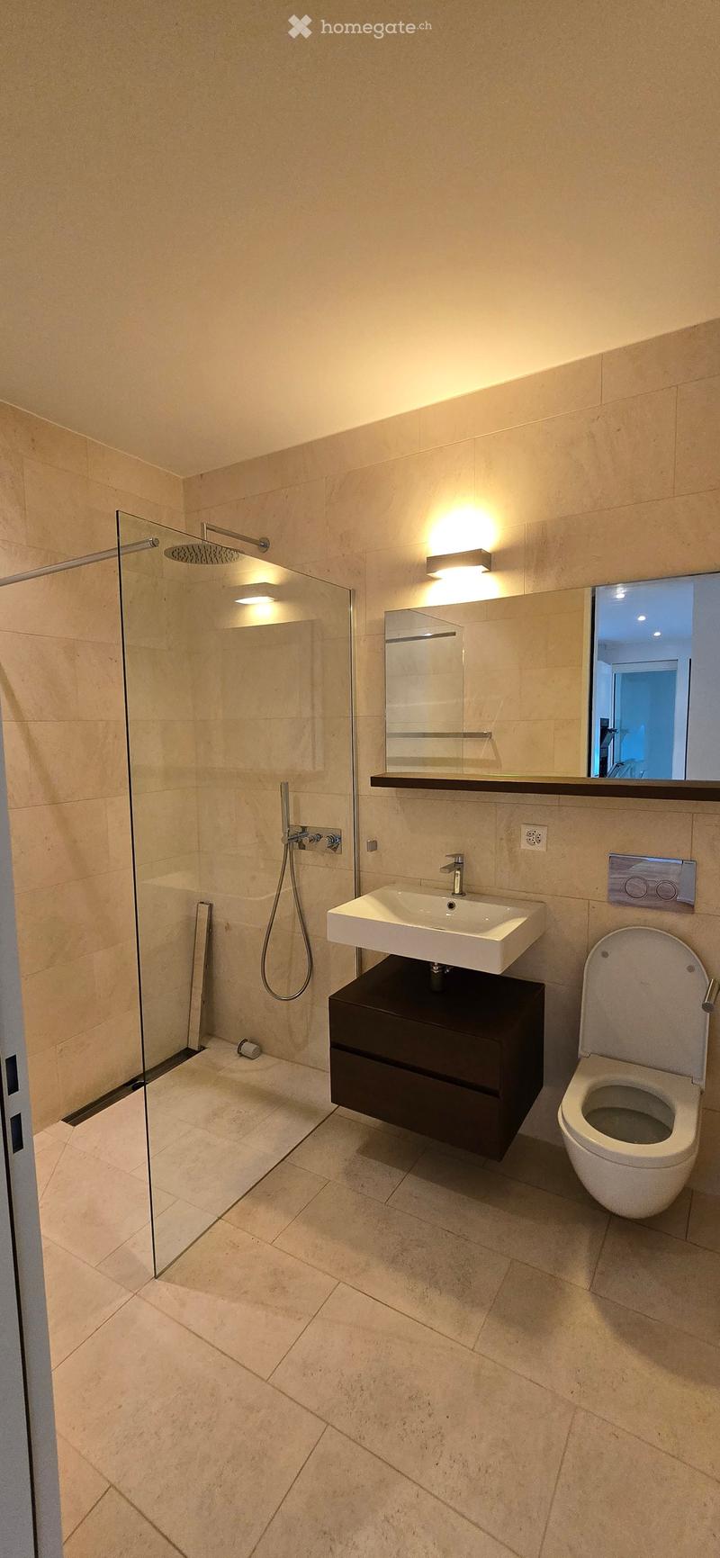 Modern bathroom with beige tiles, a glass-enclosed shower, a floating sink with a dark wooden cabinet, and a toilet.