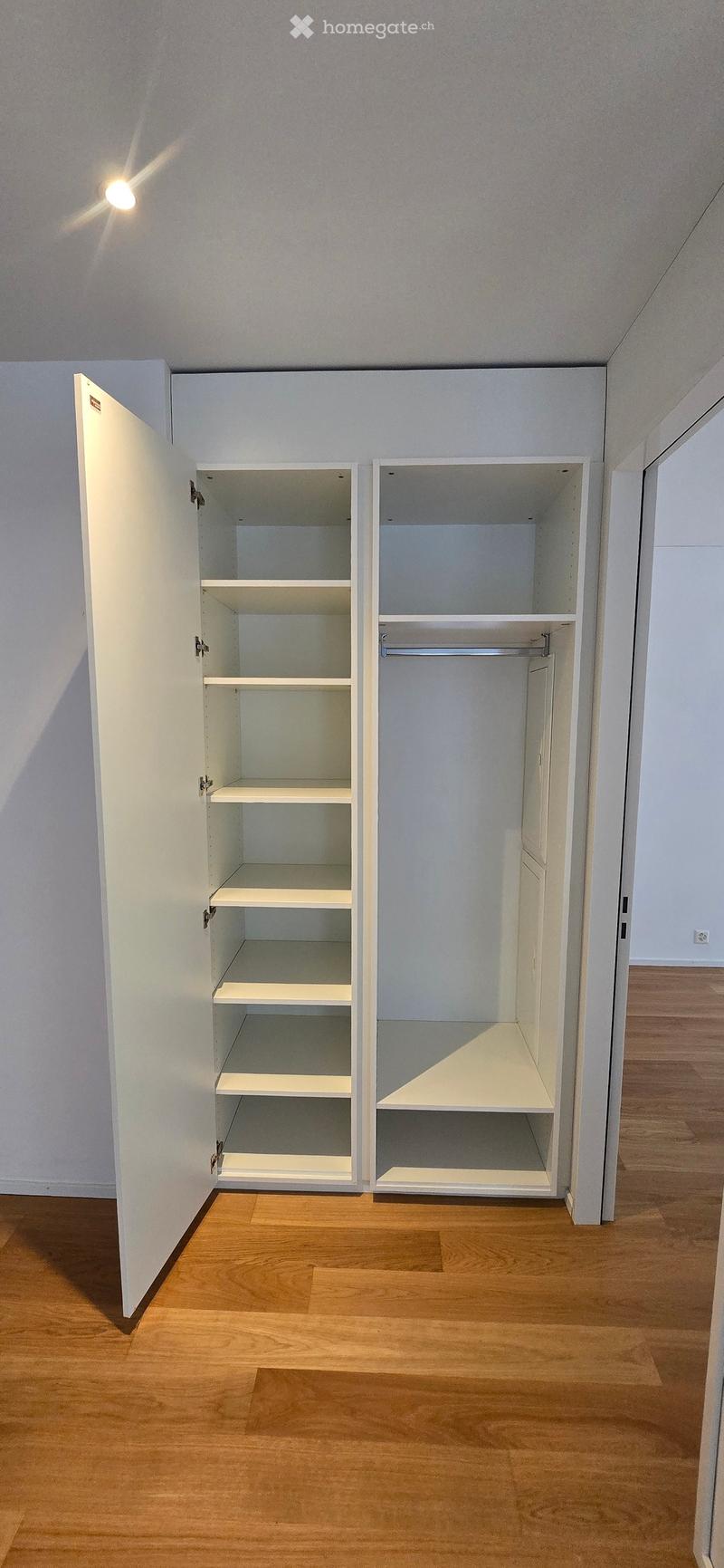 Empty room with wooden flooring, white walls, and built-in white shelving units with multiple shelves and a hanging rod.