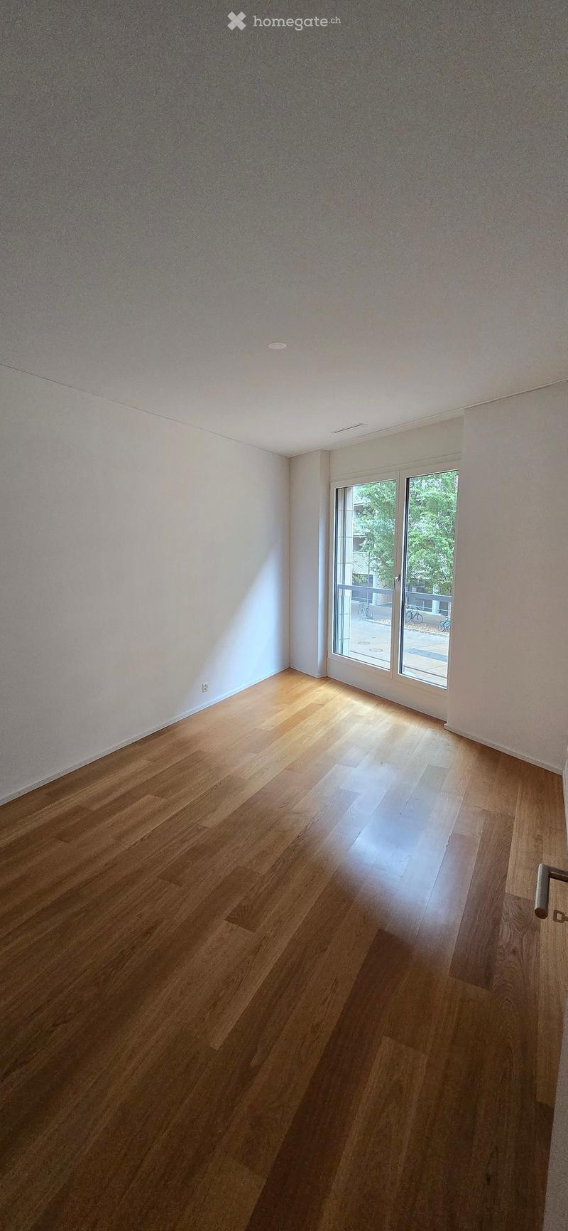 Empty room with wooden flooring and white walls, featuring a large sliding glass door leading to an outdoor area.