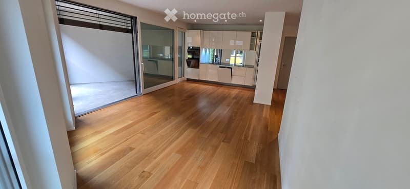 Empty room with light wooden flooring, white walls, and large glass sliding doors leading to a balcony.