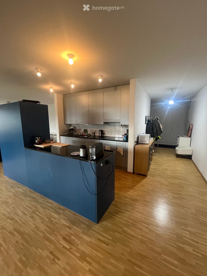 Modern kitchen with wooden flooring, white cabinets, and a blue kitchen island. Includes a microwave, stools, and various kitchen appliances.