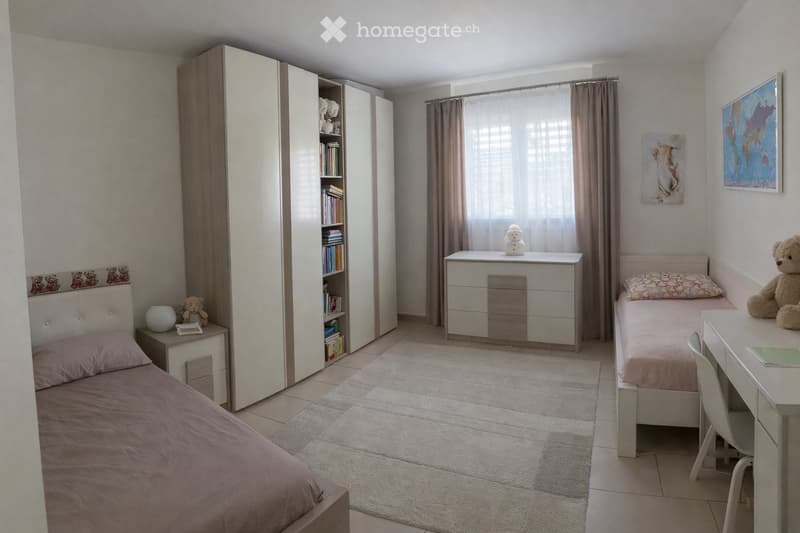 Cozy bedroom with two single beds, a large wardrobe, a desk with a chair, and decorative items including a globe and artwork on the walls.
