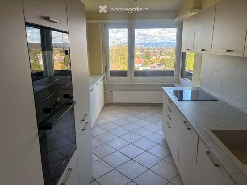 Modern kitchen with white cabinets, tiled floor, large windows offering a scenic view, and built-in appliances including an oven and countertop.