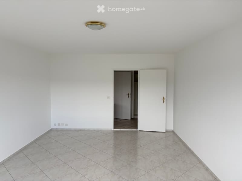 Empty room with white walls, tiled floor, and a single ceiling light fixture. A closed door and an open doorway lead to another space.
