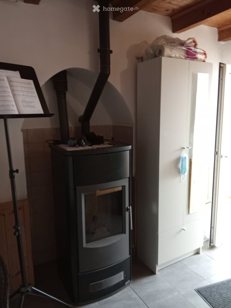 A cozy room with a modern black wood-burning stove, a white cabinet, a small stool, and a music stand with sheet music.