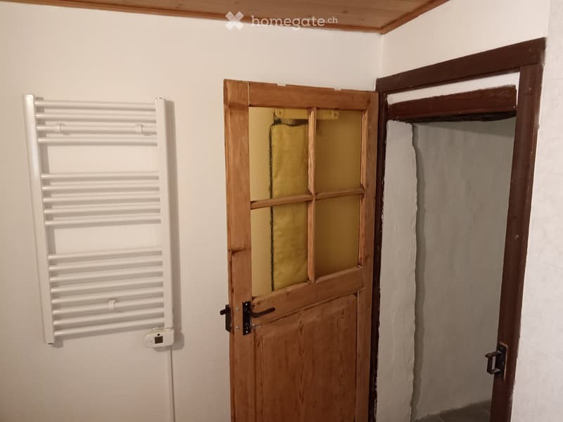 Empty hallway with white walls, wooden doors, and a towel rack on the left side.
