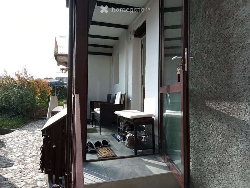 A small, furnished entryway with a tiled floor, a chair, a small table, and a shoe rack holding shoes and bags.