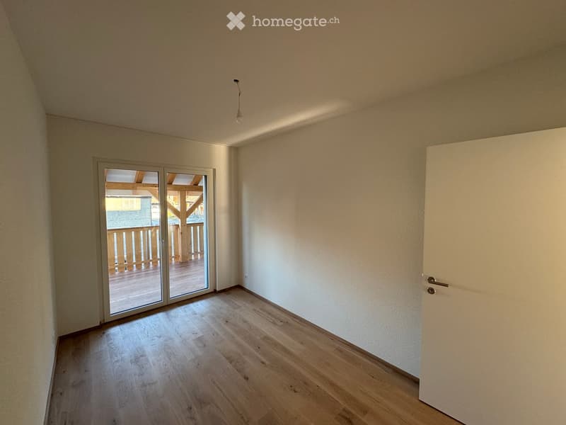 Empty room with light wooden flooring, white walls, and a sliding glass door leading to a wooden deck and outdoor area.