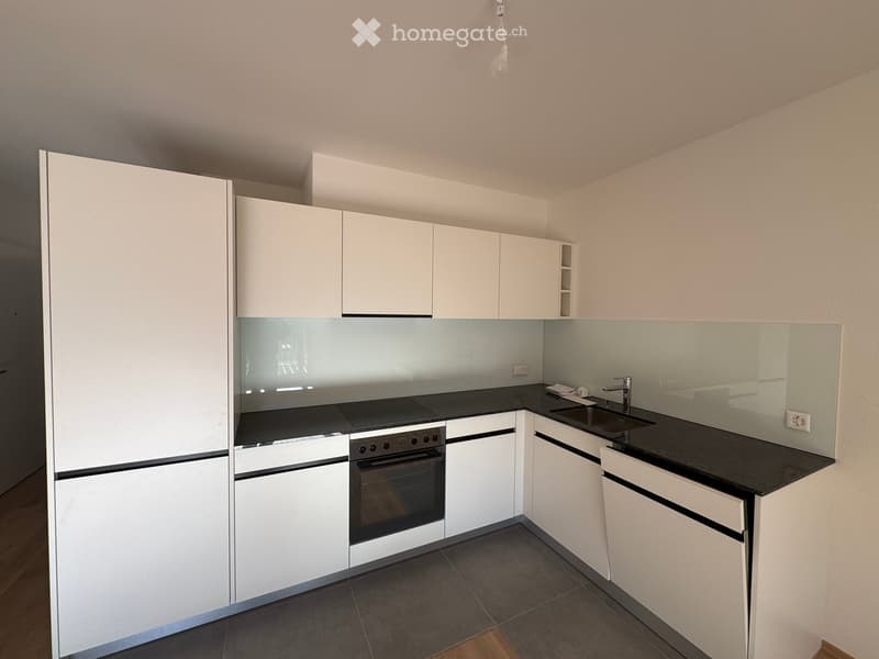Modern kitchen with white cabinets, black countertops, and stainless steel appliances including an oven and sink.