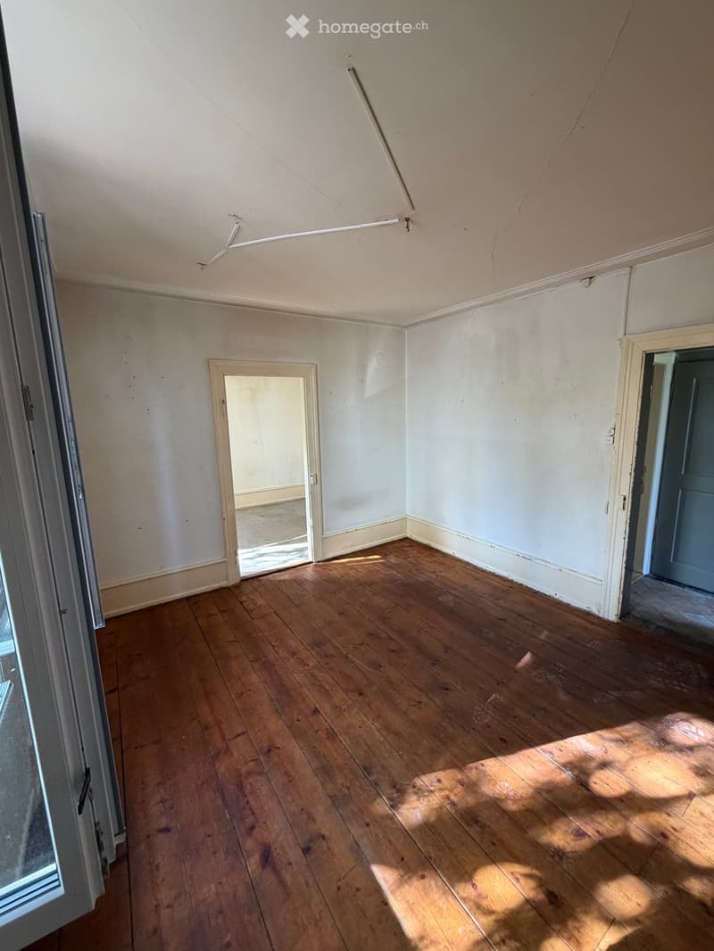 Empty room with wooden flooring, white walls, and two doors, one leading to another room.