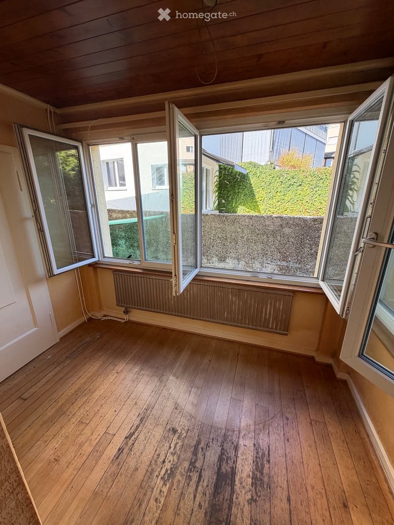 Empty room with wooden flooring, large windows, radiators, and a wooden ceiling.