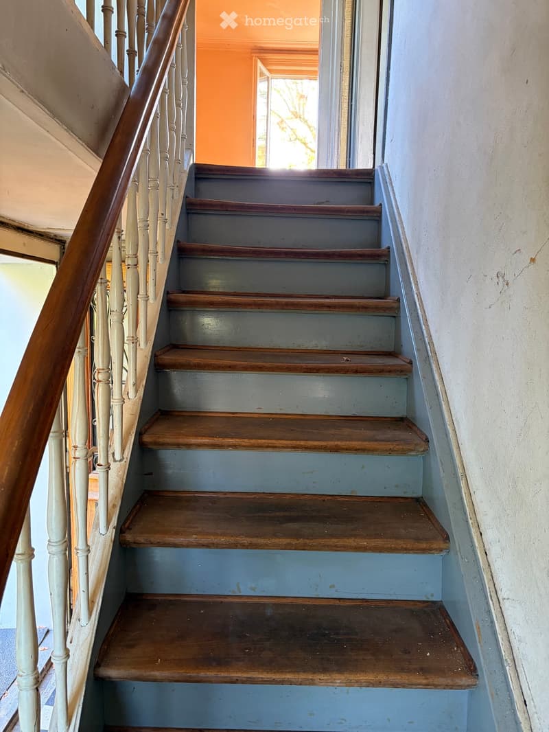 Wooden staircase with blue painted risers and white painted balusters, leading to an open doorway with natural light.