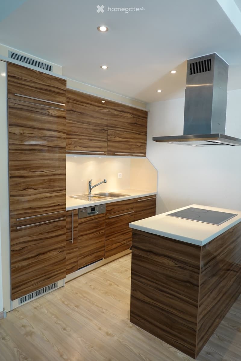 Modern kitchen with wooden cabinets, a central island, and built-in appliances including a dishwasher and induction cooktop.
