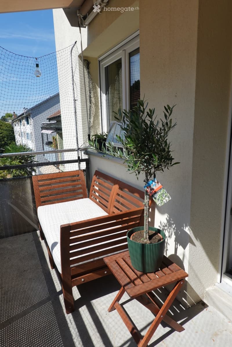 Balcony with a wooden bench, small wooden table, and potted plant. The balcony has a metal railing and is enclosed with a net.