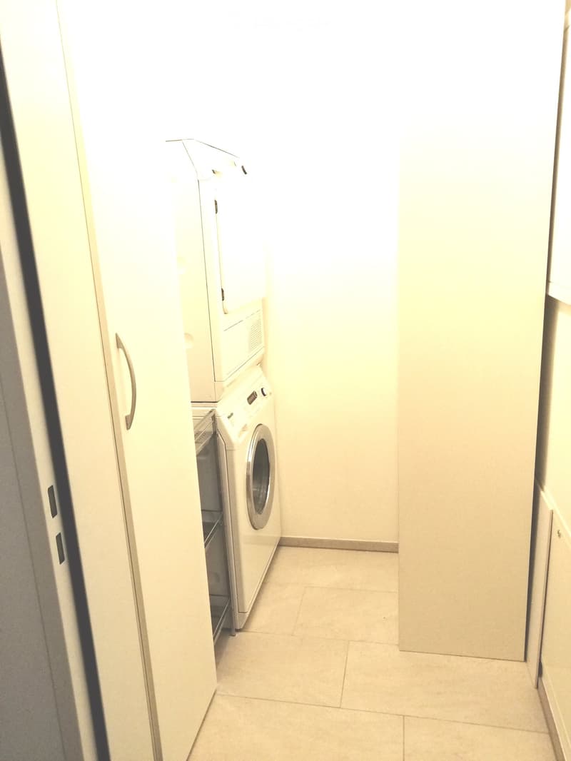 Small, well-lit bathroom with a white washing machine and matching cabinets.