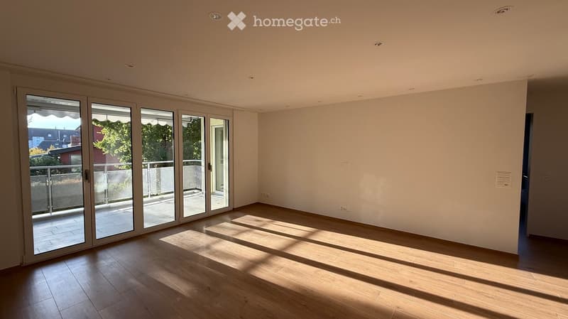 Empty room with wooden flooring, large sliding glass doors leading to a balcony, and natural light streaming in.