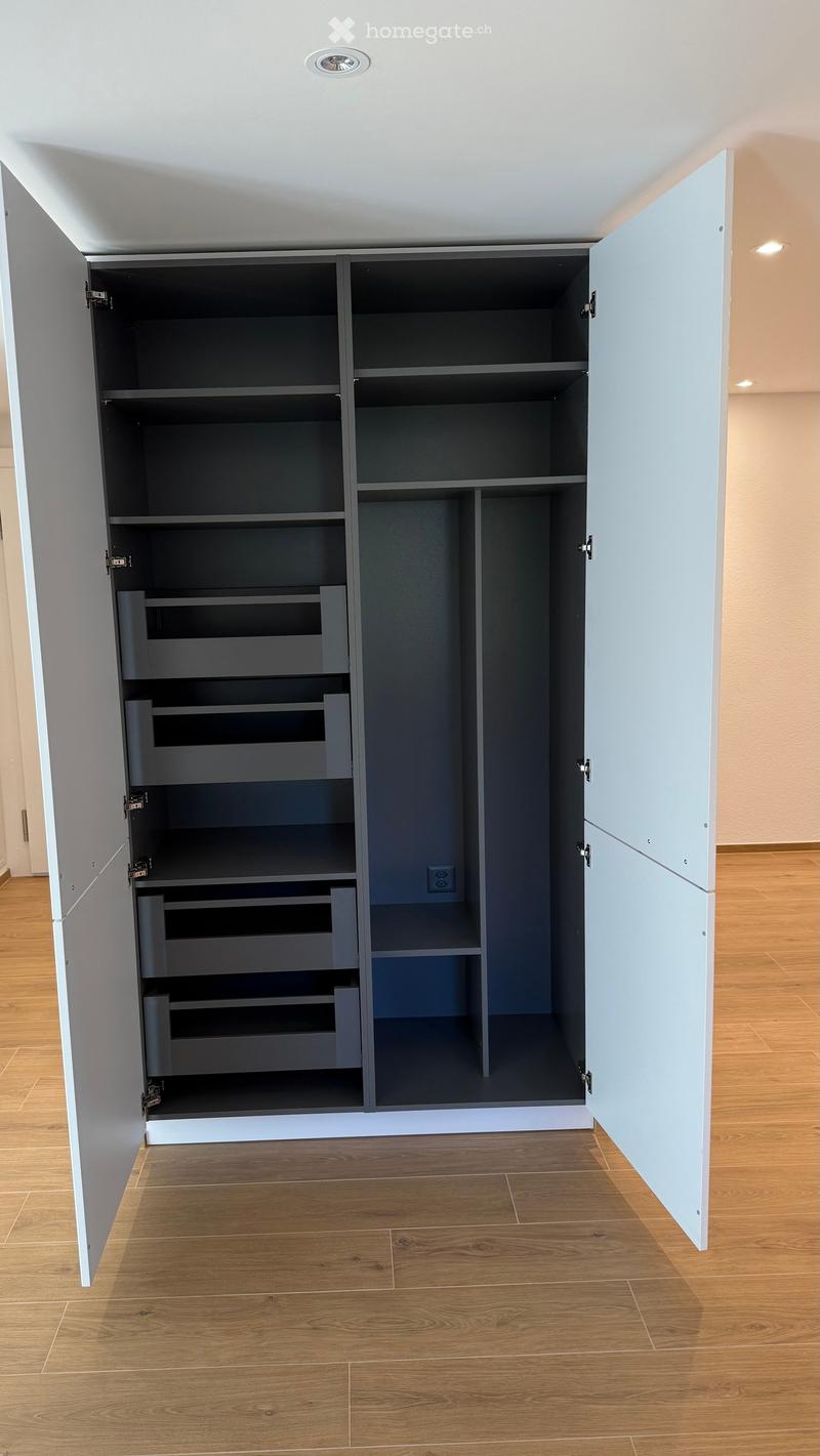 Empty room with wooden flooring and built-in storage unit with open shelves and drawers.