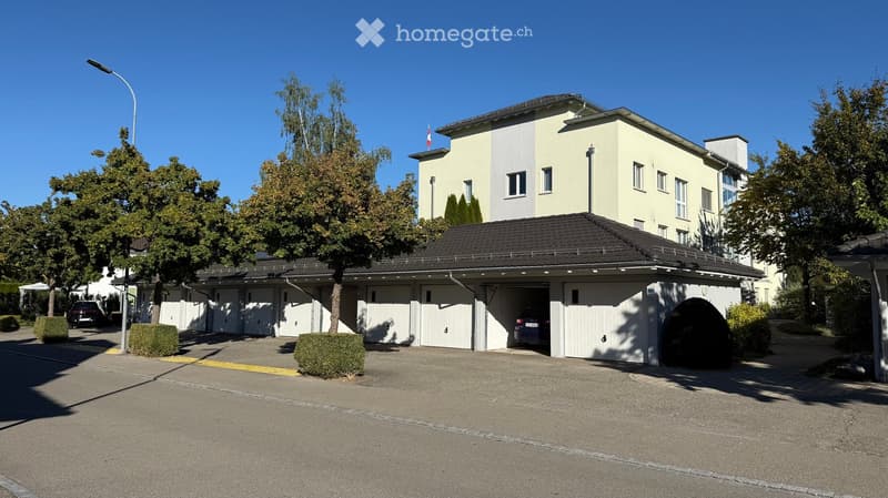 Two-story building with a large attached garage, multiple garage doors, and a driveway with parked cars.